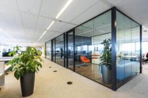 Modern kantoorinterieur aan de Johan Huizingalaan met glazen vergaderruimtes, planten en een oranje loungestoel.